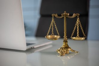 Balança dourada da justiça sobre uma mesa, ao lado de um computador portátil.