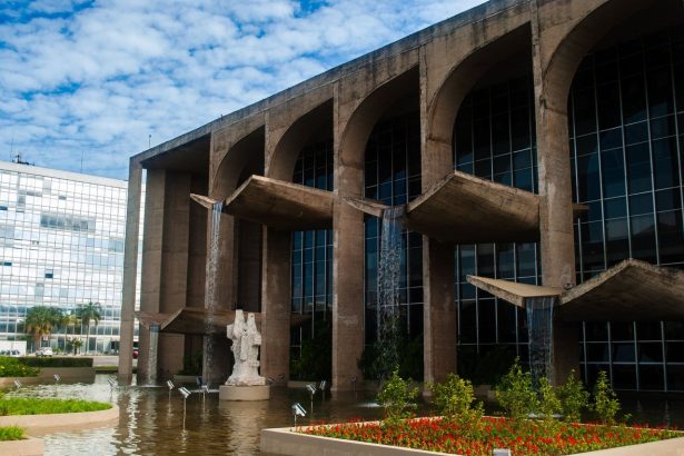 Edifício de arquitetura moderna em Brasília, refletido em um espelho d’água sob céu claro.