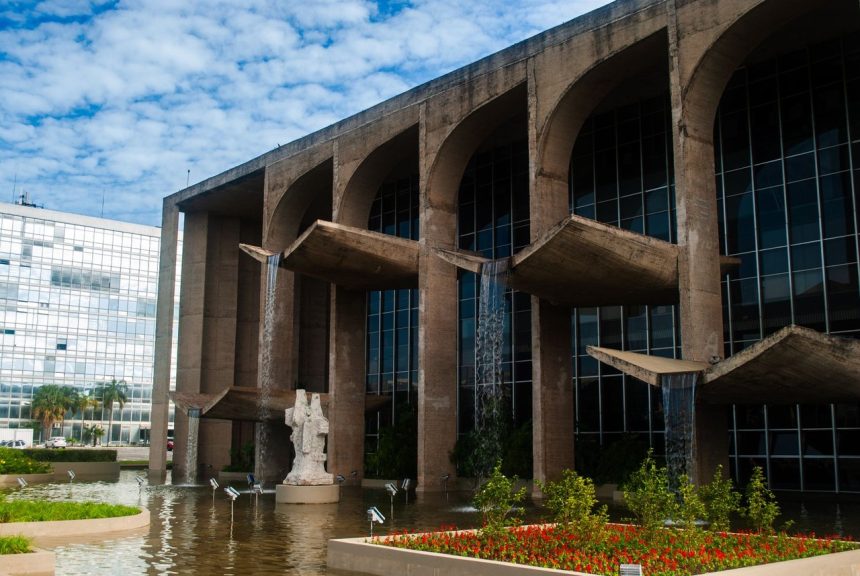 Edifício de arquitetura moderna em Brasília, refletido em um espelho d’água sob céu claro.