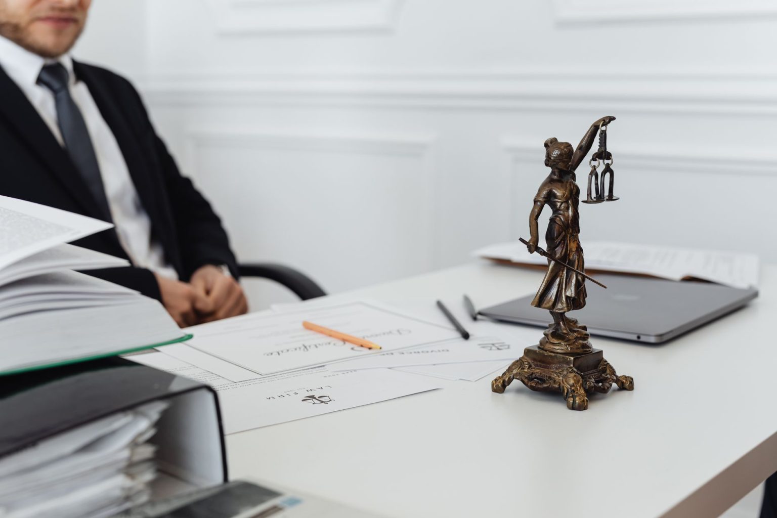 Mesa de trabalho jurídico com documentos, notebook e uma estátua da Justiça.