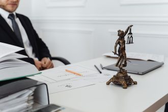 Mesa de trabalho jurídico com documentos, notebook e uma estátua da Justiça.