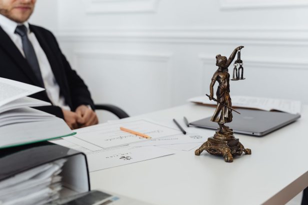 Mesa de trabalho jurídico com documentos, notebook e uma estátua da Justiça.