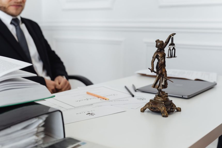 Mesa de trabalho jurídico com documentos, notebook e uma estátua da Justiça.